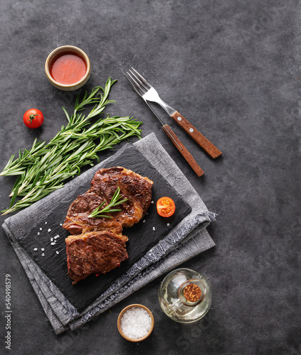 BBQ beef steak grill with sauce,tomatoes and rosemary on black slate on dark background.