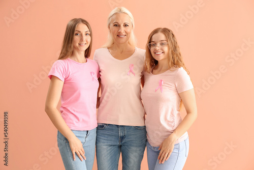 Beautiful women with pink awareness ribbons hugging on color background. Breast cancer concept