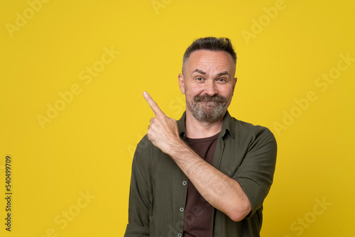50s handsome man pointing with finger up to copy space smiling and happy wearing casual green shirt standing over isolated yellow background