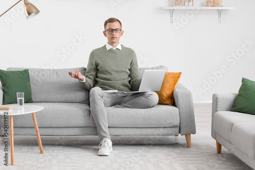 Young man with laptop meditating on sofa at home