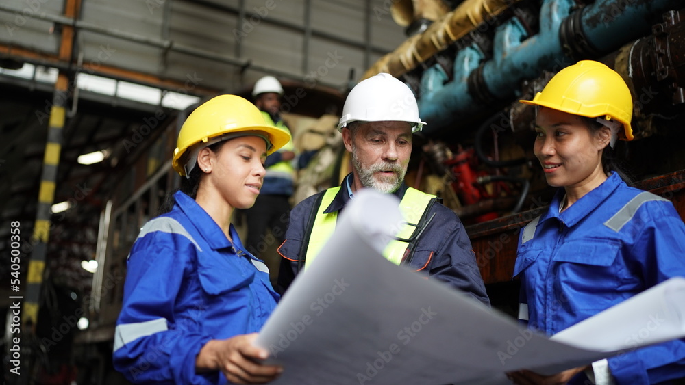 Engineers in discussion in machine maintenance in factory. Group of Industrial Engineers with Blueprint against trains and machinaries industry background. Engineers in discussion in machine maintenance in factory. Group of Industrial Engineers with Blueprint against trains and machinaries industry background.