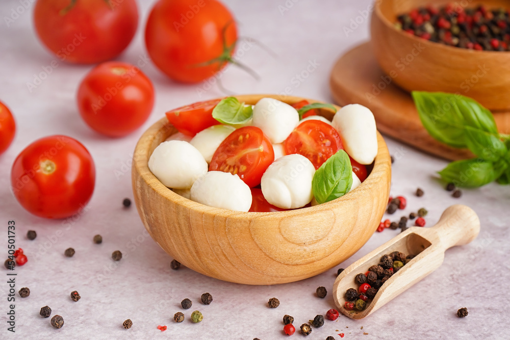 Wooden bowl with tasty mozzarella cheese, tomatoes and spices on light background Wooden bowl with tasty mozzarella cheese, tomatoes and spices on light background