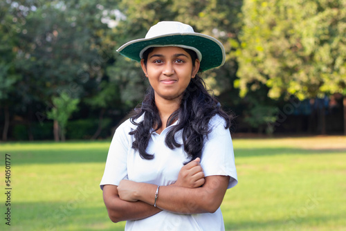 a girl wearing cricket uniform and cap standing in outdoor