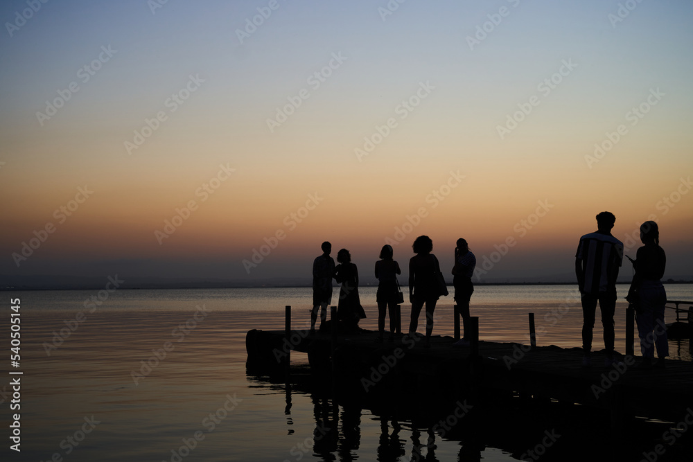 Fototapeta premium Tourists waiting to take pictures at wooden dock in Albufera lake in Valencia at sunset