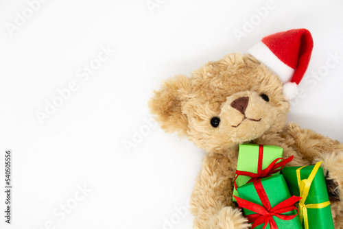 Teddy bear in Santa Claus hat holds gift boxes. Copy space