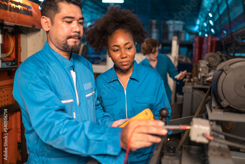 Engineer senior asian man and african woman wearing safety helmet working and checking machine automotive part warehouse. Factory for the manufacture and electric processing.