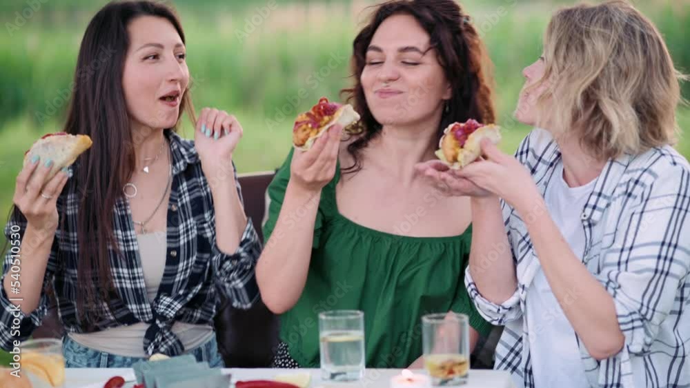 Three young Caucasian women eat tacos in nature with great appetite.