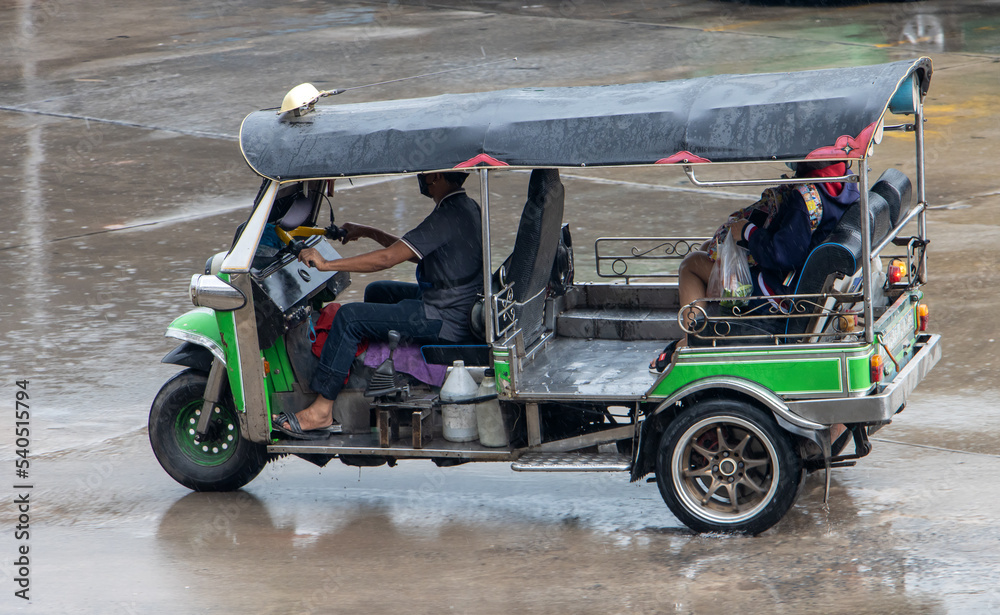 Traditional motorized tricycle - tuk tuk rides on the road in the rain, Thailand