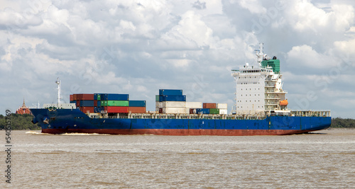 A container ship loaded with containers sails alongside the shore photo
