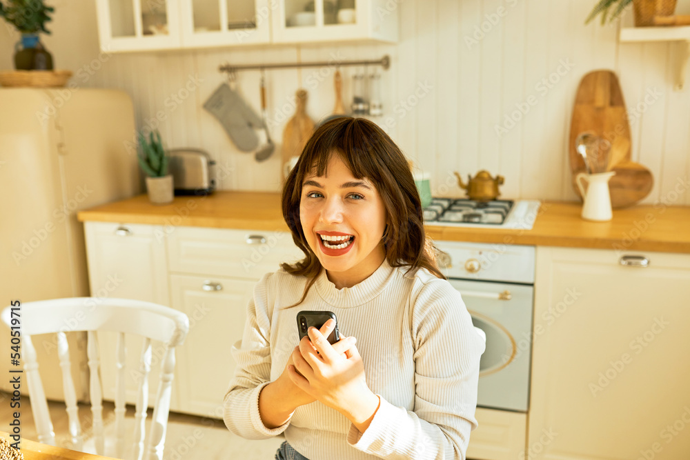 Happy cheerful young brunette wearing red lipstick, holding smartphone tightly after reading message with news of her winning lottery or special offer, looking at camera with excited, surprised face Happy cheerful young brunette wearing red lipstick, holding smartphone tightly after reading message with news of her winning lottery or special offer, looking at camera with excited, surprised face