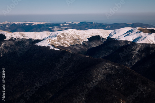 Panoramic view over the ski slope Poiana Brasov ski resort in Transylvania, Pine forest covered in snow on winter season,Mountain landscape in winter with the Bucegi Mountains in the background. photo