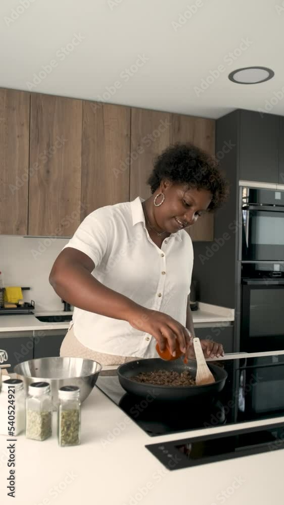 Young cuban woman adding tomato sauce to cook minced beef and garlic in a pan to prepare cuban style stuffed potatoes. Young cuban woman adding tomato sauce to cook minced beef and garlic in a pan to prepare cuban style stuffed potatoes.