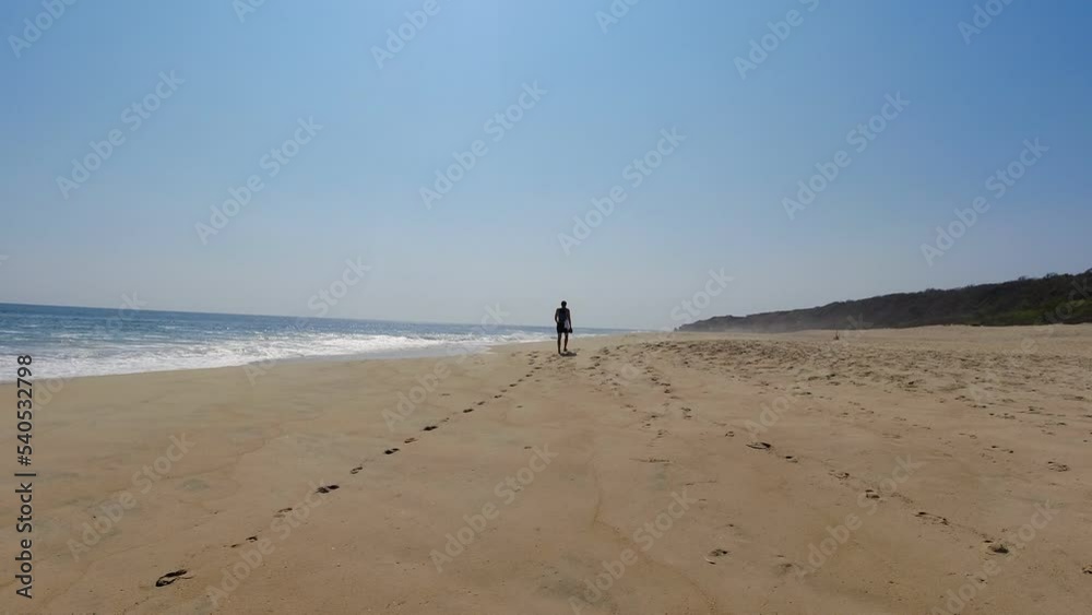 Tourist in beach outfit walks towards the horizon on a lonely beach Tourist in beach outfit walks towards the horizon on a lonely beach