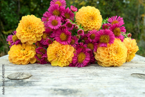 A bouquet of autumn flowers with yellow dahlias and pink asters lies on a wooden table
