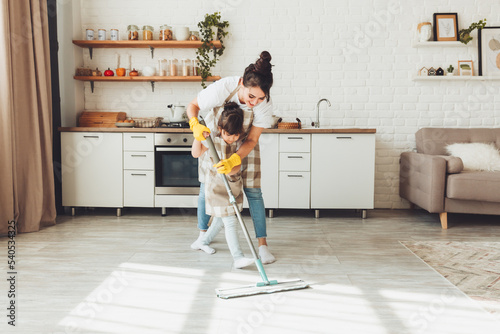 a little daughter and her mom clean the house, a child washes the kitchen floor, a cute little helper girl cleans the floor with a mop, a happy family cleans the room. photo