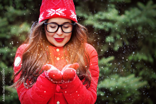 Woman wearing red jacket and hatl blowing snow off photo