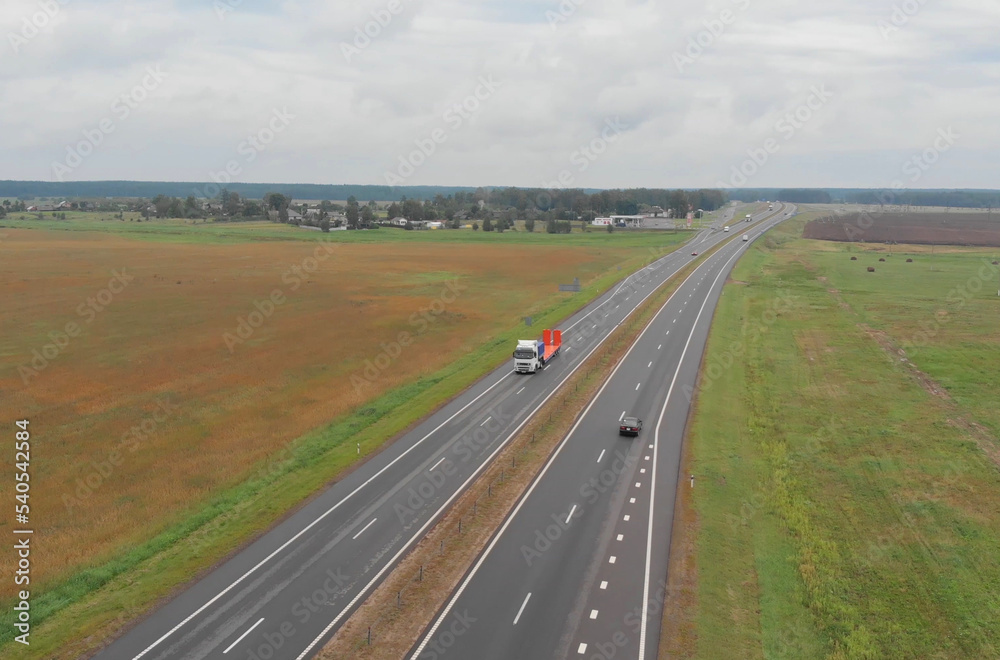 Top view of a truck and cars moving along the asphalt road along the fields.