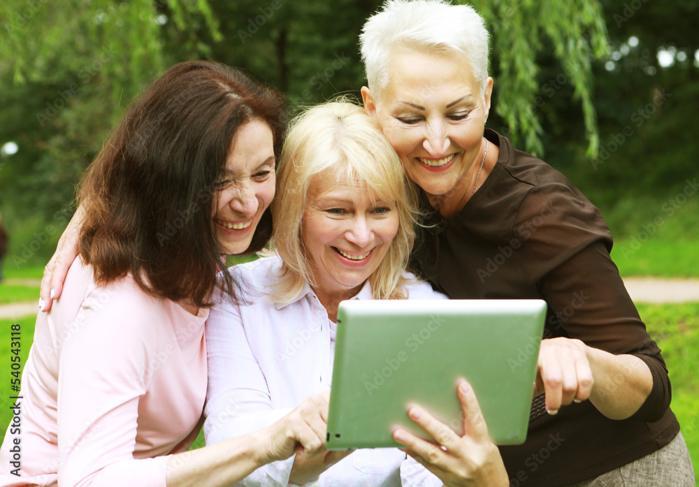 Charming old women laugh merrily and look at the screens of tablet. Having fun in retirement on a summer afternoon. Charming old women laugh merrily and look at the screens of tablet. Having fun in retirement on a summer afternoon.