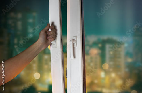 Hand opens the window with a view of the night city