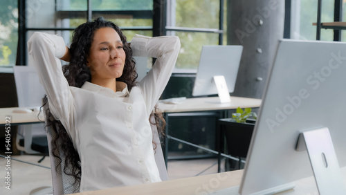 Relaxed contented young woman sitting at workplace enjoying finished work happy calm businesswoman leaning back in chair holding hands behind head relaxing resting daydreaming taking break at office