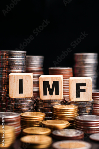 Stacks of gold coins with the letters IMF (International Monetary Fund) on a wooden cube. Business concept. vertical	                            