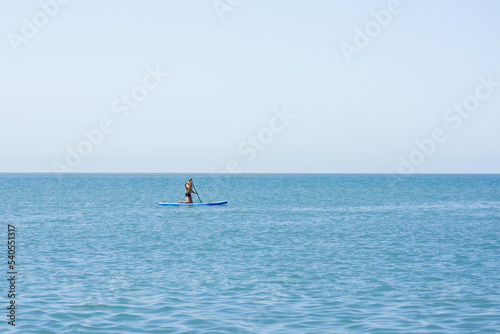 A man alone in a life jacket sits on a SUP board with an oar. Lonely swimmer in the open sea.