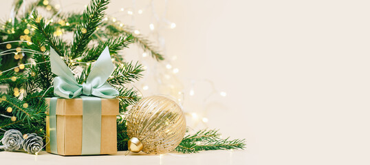 Gift box with green bow and crystal golden bauble. christmas tree and lights background, copy space. Winter holidays celebration concept.
