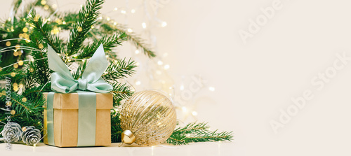 Gift box with green bow and crystal golden bauble. christmas tree and lights background, copy space. Winter holidays celebration concept.