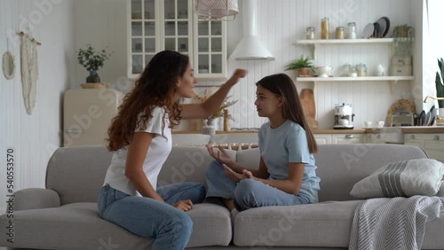 Aggressive Caucasian woman scolding teen girl and yelling loudly at child for bad grades or school reprimand. Mother sits on couch quarrels with daughter after conversation with teacher or amiss act photo