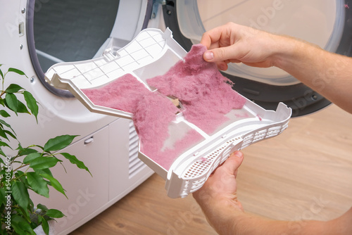 A man holds a dirty dryer filter. A man collects lint, hair, wool from the filter of a drying machine. Red lint on the dryer filter. Dirty filter dryer.