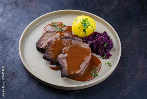 Traditionell geschmorter Sauerbraten vom Rind mit Blaukraut und Kartoffelklößen in würziger Dunkelbiersoße serviert als close-up auf einem Nordic design Teller photo