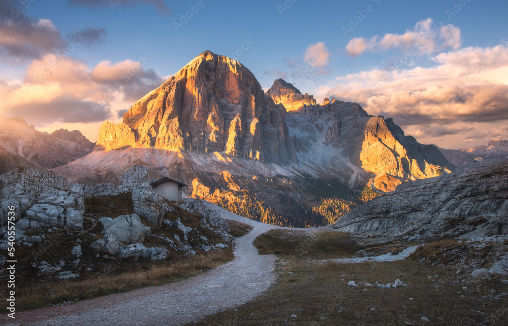 Mountains and beautiful sky with colorful clouds at sunset in autumn. Colorful landscape with mountain peaks, path, stones, grass, blue sky with clouds in fall. High rocks in Dolomites, Italy. Nature