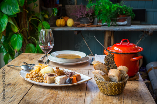 Cocido Madrileño, a traditional Spanish meal, served with soup, chickpeas, bacon, chorizo, black pudding, ham bone, boiled potato, cabbage, bread and a glass of red wine. photo