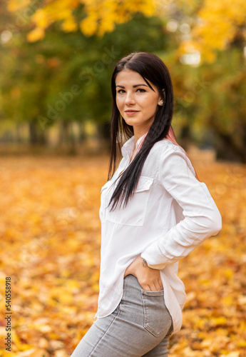 Fototapeta Naklejka Na Ścianę i Meble -  Beautiful female office worker walks in autumn park during lunch time orange, yellow leaves trees on background, walking outdoors. Relaxation, enjoying, solitude with nature. Stress relief. Vertical
