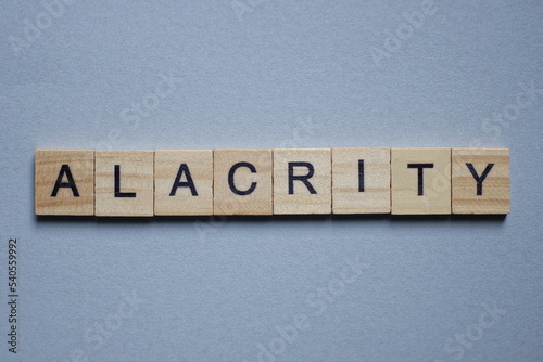 text the word alacrity from brown wooden small letters with black font on an gray table photo