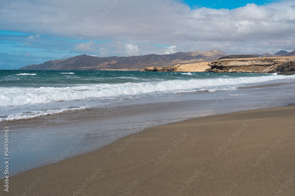 Beach with dark sand, waves of Atlantic Ocean and harsh volcanic mountains in the background. La pared - Fuerteventura (canaries islands)