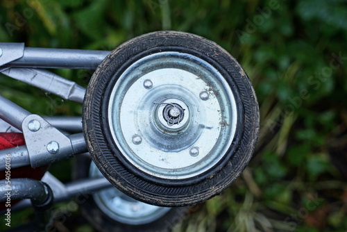 small dirty gray black metal and plastic wheel on a trolley outdoors on a green background