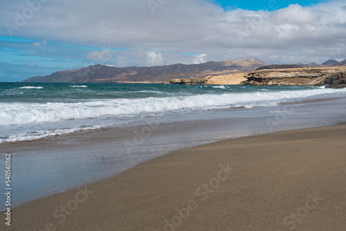 Beach with dark sand, waves of Atlantic Ocean and harsh volcanic mountains in the background. La pared - Fuerteventura (canaries islands)