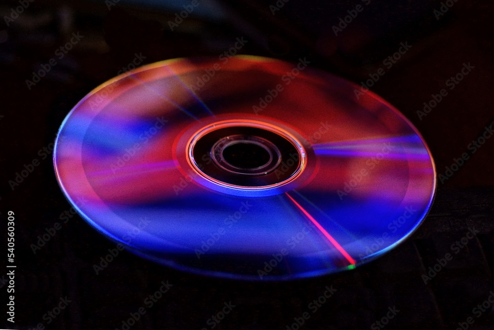 one old plastic compact disc with a bright red blue colored reflection on a black background one old plastic compact disc with a bright red blue colored reflection on a black background