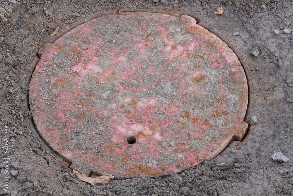 one old red rusty sewer hatch on the road on the ground in the street