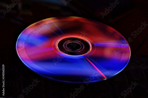 one old plastic compact disc with a bright red blue colored reflection on a black background