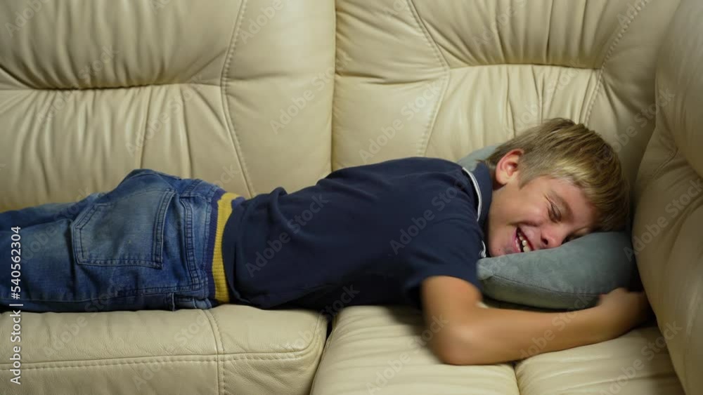 Tired exhausted teen falling down on sofa and smiling at home after hard working day. Cute cheerful teen boy lying on couch while taking nap at living room Tired exhausted teen falling down on sofa and smiling at home after hard working day. Cute cheerful teen boy lying on couch while taking nap at living room