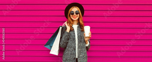 Portrait of beautiful smiling stylish woman with shopping bags wearing gray coat, hat on colorful pink background © rohappy