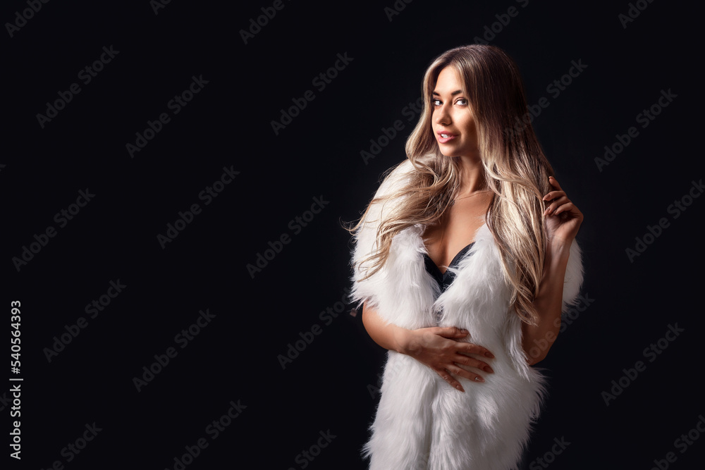 Beautiful blonde girl posing in luxurious white fur cape while standing on black background. Fashion Beautiful blonde girl posing in luxurious white fur cape while standing on black background. Fashion
