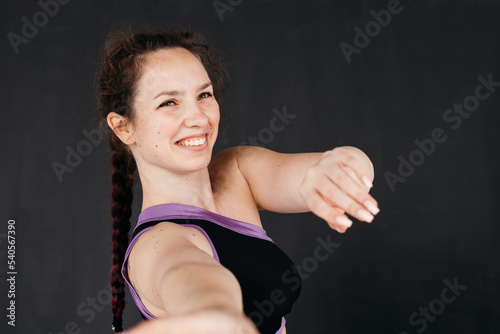 A pretty brunette girl smiling. Young sports woman stretches her arms towards the camera. Dark backgroud. Femininity concept.