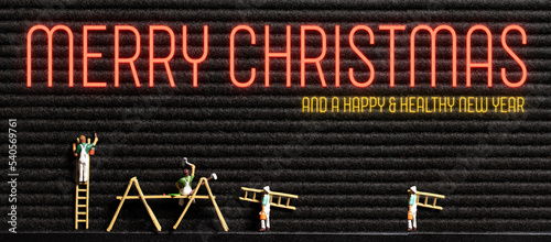 neon message MERRY CHRISTMAS AND A HAPPY AND HEALTHY NEW YEAR on a letter board with tiny painter figures #540569761