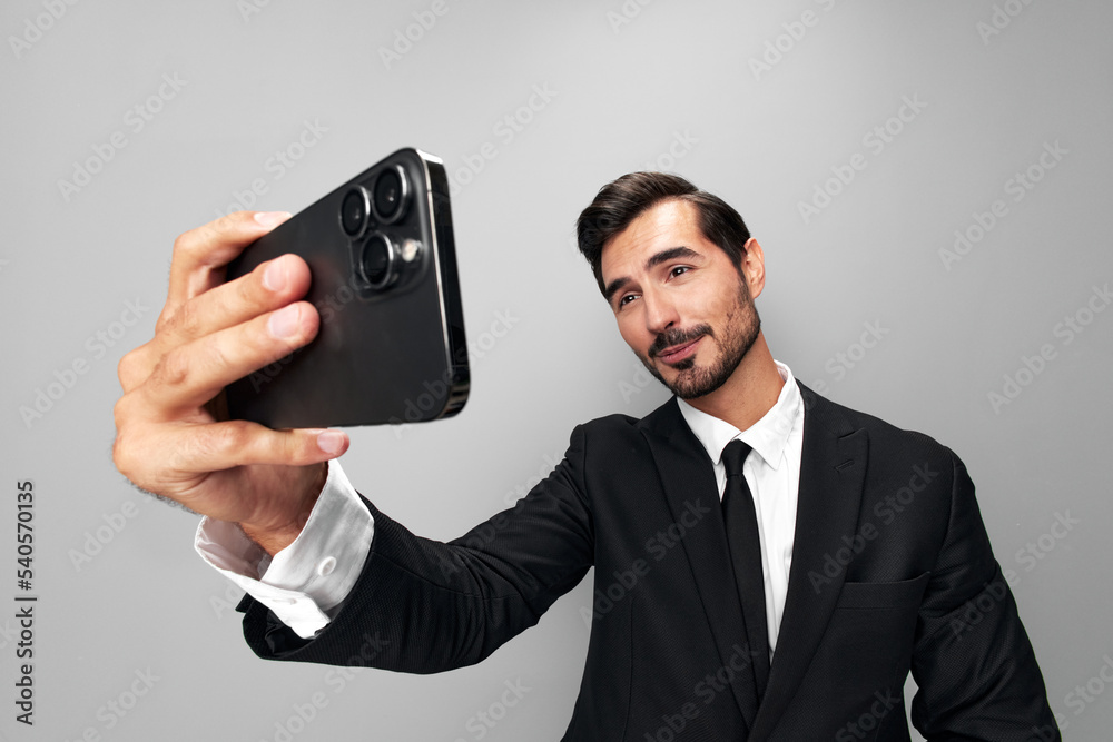 Man businessman in suit takes selfies on phone posing in front of smartphone camera with smile with teeth happy win on gray background close-up face wide camera angle Man businessman in suit takes selfies on phone posing in front of smartphone camera with smile with teeth happy win on gray background close-up face wide camera angle