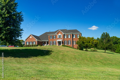 Luxurious country house on hill against a blue sky. Green lawn and landscaping.