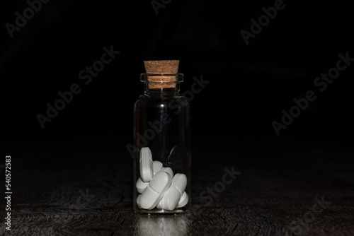 Pills in the glass phial on the dark background