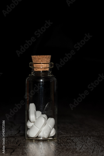 Pills in the glass phial on the dark background
